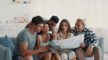 A group of diverse friends gathers in a sunny living room, excitedly discussing their travel plans while studying a large map, sharing laughter and ideas. video