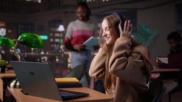 Girl studying in the library to obtain her diploma with focus music on headset, using the academic database for research. Student generating creative ideas for the bachelor paper. Camera B. video