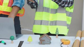 Two people in safety vests standing next to a laptop and a model of a house video