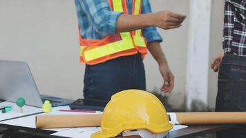 Two men in hard hats standing next to a laptop and construction materials video