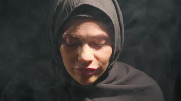 woman wearing black hijab sits calmly lost in thought amidst smoky atmosphere and washes her face. dim light creates serene and contemplative mood perfect for reflection, washes her face video