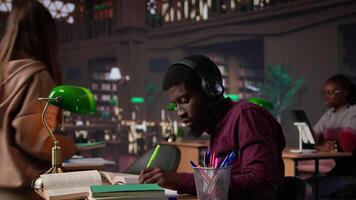 Black guy using study music to help with deep focus for academic success, consulting the campus university database to find reliable sources. Male college student fights for diploma. Camera B. video