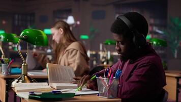Male student listening to ambient study music on headset and collecting data from a book, focusing on school projects. Enjoying focus ambience music to finish a school assignment. Camera A. video