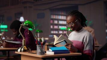 Black girl focuses on her exam preparations in the campus library, takes notes on her laptop from reference books in a peaceful study setting. Girl uses the general database materials. Camera A. video