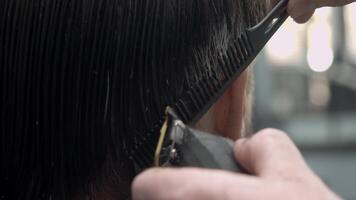 A barber employs a trimmer to create a sharp outline and shape the hair around the brunette client s temples in the barbershop. Close up video