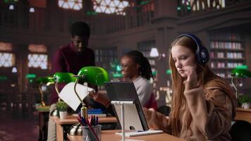 Young female adult listening to therapy music and working on her bachelor paper, using ambient sounds to help her focus in the university library. Student does academic research. Camera B. video