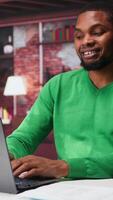 Vertical Black remote employee in home office using laptop for web assignments, preparing presentation slides and working on data layouts. Young teleworker finishing company project. Camera B. video