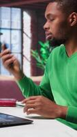 Vertical Smiling man at home having friendly conversation with friends over phone call on smartphone. African american guy having fun catching up with people on telephone line, freelance. Camera B. video