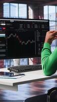 Vertical Day trader uses computer to purchase stocks that might perform well and selling ones that might drop in value. Forex trader browsing though stock exchange portfolio pages at PC desk. Camera B. video