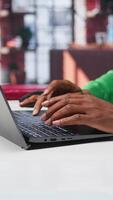 Vertical Freelancer creating articles content for his online blog at home desk, writing and working on storytelling with his laptop. Black guy composes social media posts, multitasking. Camera B. video