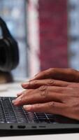 Vertical Freelancer creating articles content for his online blog at home desk, writing and working on storytelling with his laptop. Black guy composes social media posts, multitasking. Camera A. video