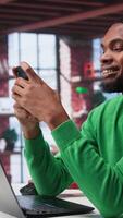 Vertical Man at home using smartphone to compose social media posts, producing content as a freelancer. African american guy monitoring profile engagement using mobile phone. Camera B. video