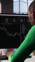 Vertical Day trader uses computer to purchase stocks that might perform well and selling ones that might drop in value. Forex trader browsing though stock exchange portfolio pages at PC desk. Camera A. video