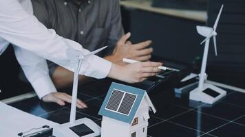 Two people working on a laptop with a model of a house and wind turbines video