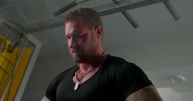 focused man is executing crossover hand raises with determination while wearing headphones. The setting is a gym highlighting strength training and fitness dedication video