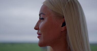 girl stands on the balcony wearing headphones and engaged in a phone conversation. She takes a refreshing sip of water enjoying the calming atmosphere around her video