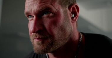 Focused on his workout a man wearing headphones is executing crossover hand raises. The close up emphasizes his determination and muscular features during the exercise video