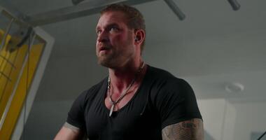 man wearing headphones concentrates on crossover hand raises with determination in a spacious gym. The workout demonstrates his dedication to fitness and strength training during the session video
