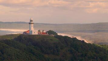 Drone footage captures the serene Byron Bay lighthouse atop lush hills with ocean views under soft evening light video