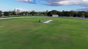 Aerial footage of groundskeepers maintaining a sports field in Gold Coast, Australia, under clear skies with lush greenery video