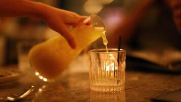 A hand pours a vibrant cocktail into a glass in a softly lit bar setting, creating a warm, inviting atmosphere video