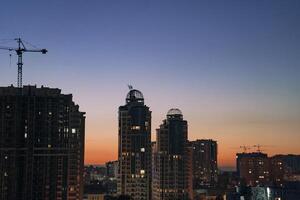Urban skyline at dusk featuring modern high-rise buildings with construction cranes silhouetted against a vibrant sunset, showcasing architectural development and city life photo