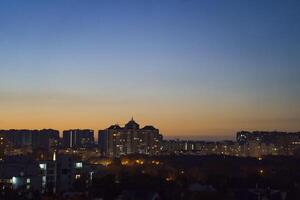Urban skyline at dusk, showcasing illuminated buildings against a gradient sky transitioning from orange to deep blue, creating a serene evening atmosphere with city lights photo