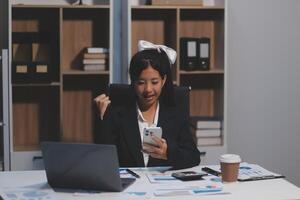 A woman in a business suit sitting at a desk with her phone and laptop photo