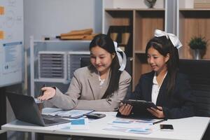 Two asian girls sitting at a desk with a laptop photo