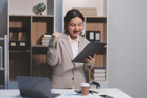 A woman in a business suit is holding a clipboard and smiling photo