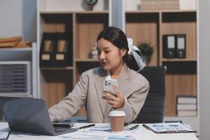 A woman in a business suit sitting at a desk with a laptop and a cell phone photo
