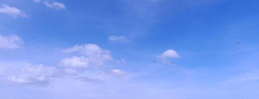 A clear blue sky with a few scattered white clouds and distant kites flying, creating a peaceful and open atmosphere. photo