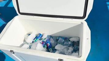 An open icebox filled with metal cola cans and plastic water bottles on a boat deck under bright sunlight video