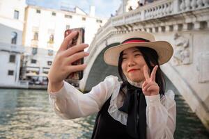 Smiling tourist does the V sign of victory under the Rialto bridge in Venice while taking a selfie photo
