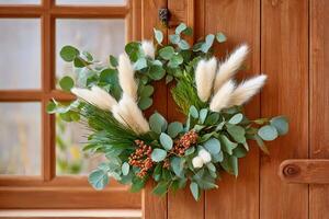 Christmas wreath hanging on a wooden door is showing eucalyptus leaves, bunny tails grass and red berries photo