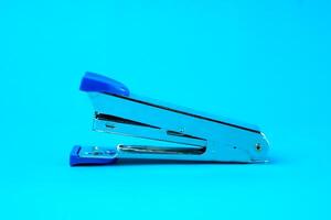 Silver metal stapler with blue plastic accents on a blue background. A compact and durable office tool designed for binding papers efficiently. Ideal for school, office, and home use. photo