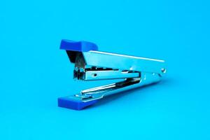 A silver metal stapler with blue plastic accents on a blue background. A compact and durable office tool designed for binding papers efficiently. Ideal for school, office, and home use. photo
