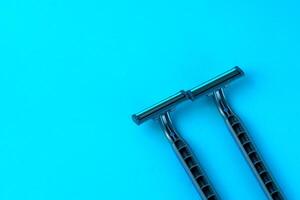 Two disposable razors with black handles on a bright blue background. Minimalist grooming tools for a smooth shave, personal care, and hygiene routine. photo
