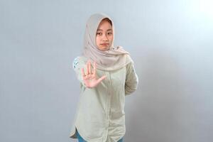 Serious young Muslim woman wearing hijab raising her hand in stop gesture while looking directly at the camera. Her firm facial expression shows assertiveness and clear boundaries. photo