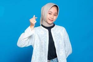 A Happy young Asian woman wearing hijab smiling warmly while showing finger heart gesture. Friendly and positive facial expression, perfect for advertising and marketing use photo