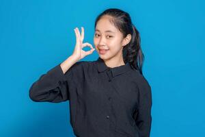 Smiling young Asian girl making an OK hand gesture with a confident and friendly facial expression. Perfect image for positive, modern advertising concepts. photo