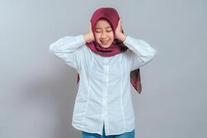 Happy young Muslim woman in hijab smiling with eyes closed, covering her ears playfully. Cheerful facial expression and lighthearted mood perfect for advertising or lifestyle content. photo