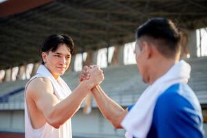 Two asian men are joining hands and locking eyes with each other on racetrack. Good sportsmanship. photo