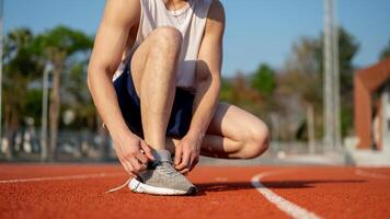 Close up of a man in white tank top crouching while tying his sneaker shoelace on the racetrack. photo