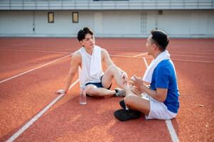 Two asian athlete men are taking a rest, sitting together on the racetrack. Jogging or Running. photo