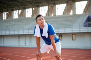 Asian man in blue t shirt is standing with hands on his knee and looking up in the sky. photo