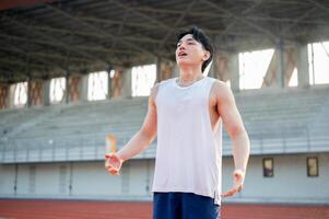 Asian man in white tank top standing with open arms and deep breathing, taking a rest after running. photo