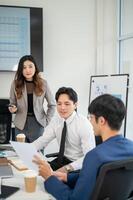 Businessman or male office worker is smiling while explaining a document to coworkers in a meeting. photo