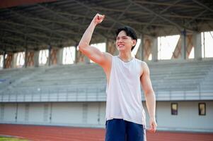 An asian man in white tank top is smiling and raising a fist while standing on racetrack. photo
