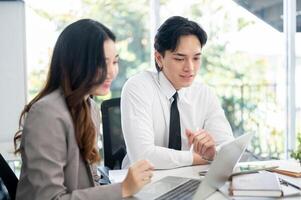 Female office worker and her male coworker is smiling while talking together at the working desk. photo